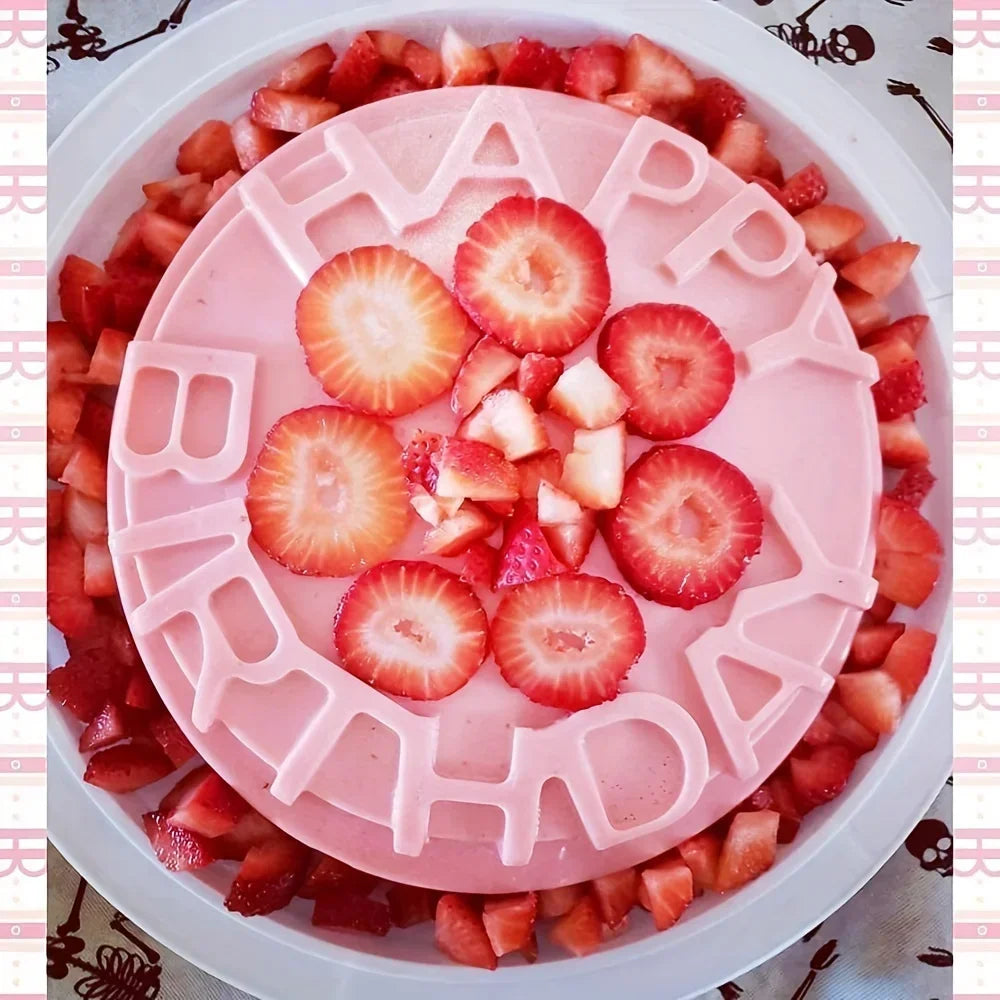 Pink silicone cake mould with "Happy Birthday" lettering, topped with fresh strawberries and surrounded by chopped fruit. Ideal for creating festive birthday cakes with personalized lettering.